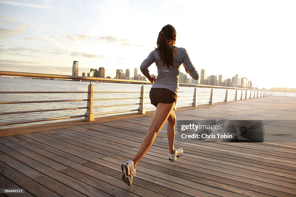 Woman running on pier in front of city skyline