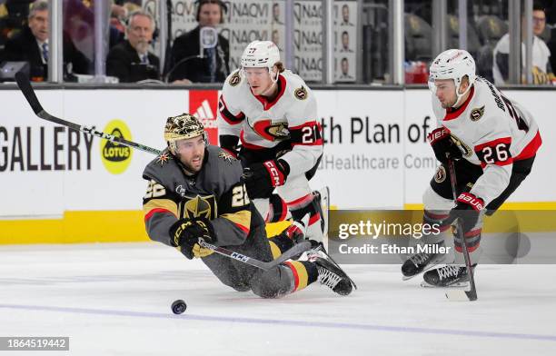 Michael Amadio of the Vegas Golden Knights tries to control the puck as he falls in front of Parker Kelly and Erik Brannstrom of the Ottawa Senators...