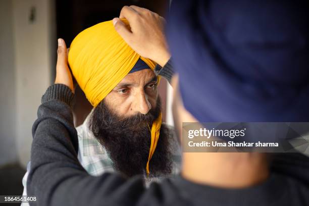 on the occasion of lohri, a young sikh man is assisting his father in tying a sikh turban. - turban stock pictures, royalty-free photos & images