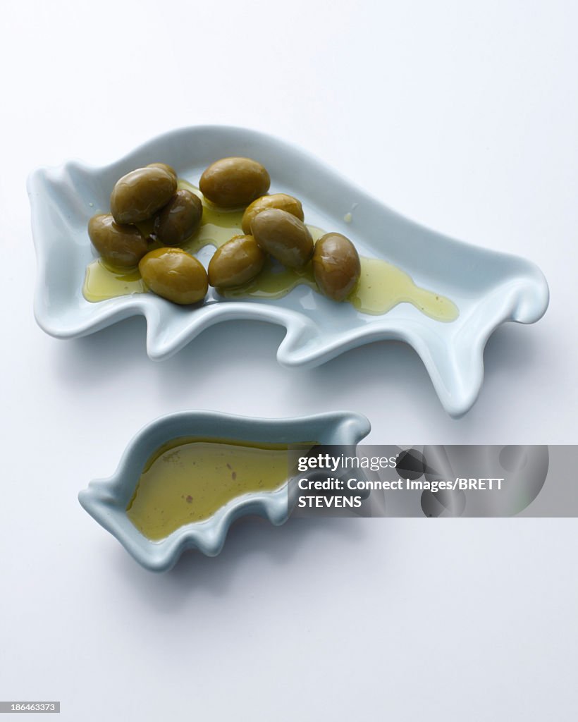 Green olives and olive oil in dishes