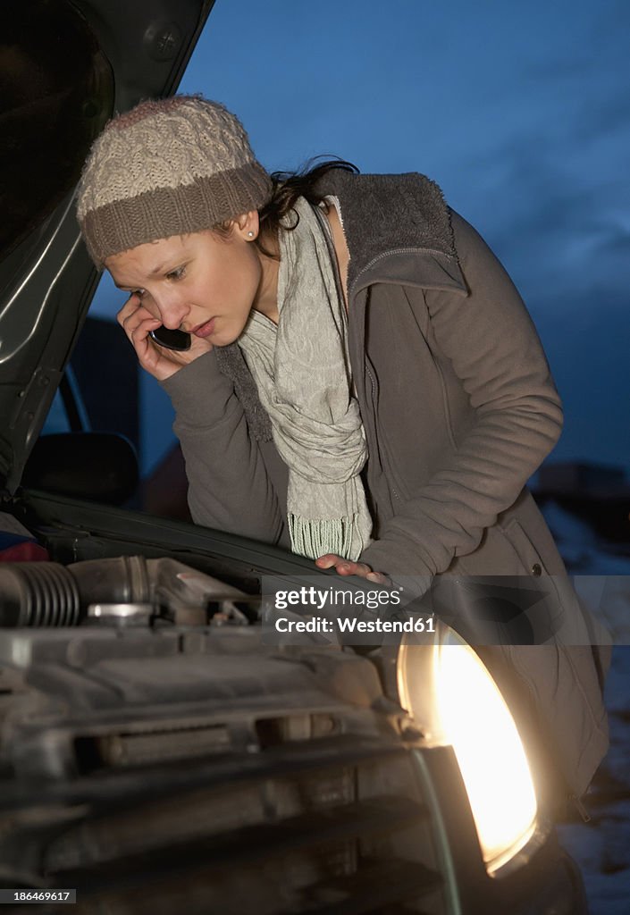Germany, Brandenburg, Young woman with car break down at night, talking on mobile phone