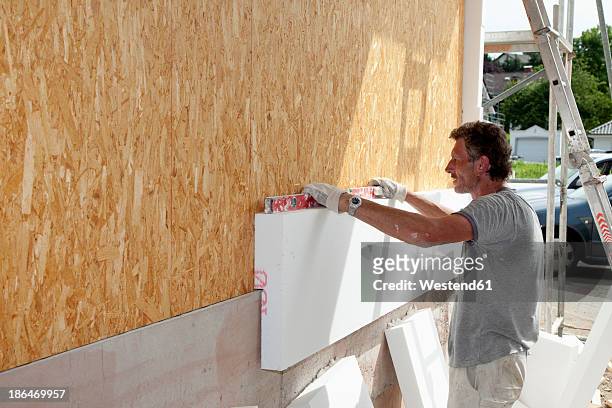 europe, germany, rhineland palatinate, man sticking polystyrene on wooden house wall - house insulation not posing stockfoto's en -beelden