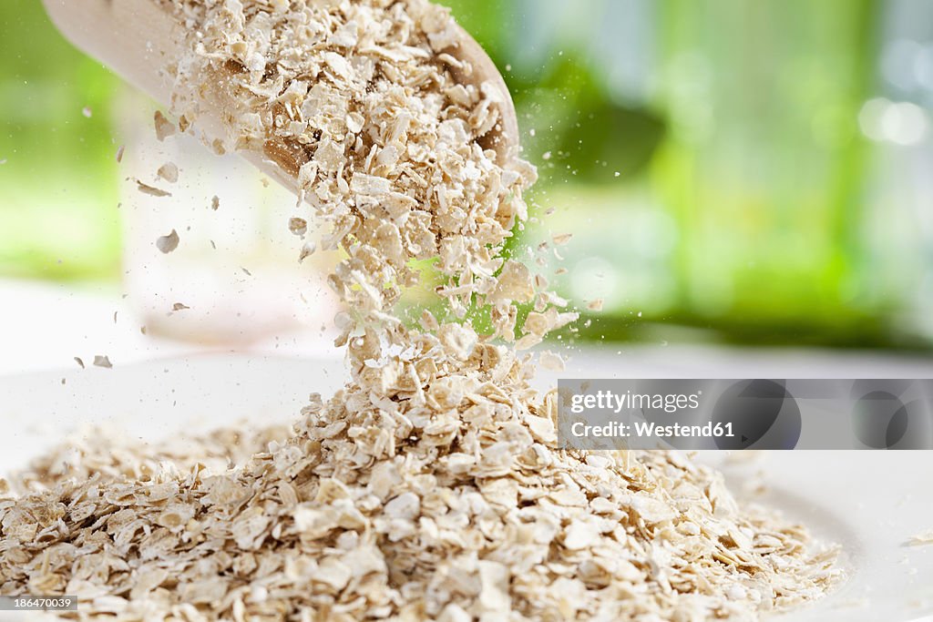 Oat flakes pouring from wooden scoop, close up