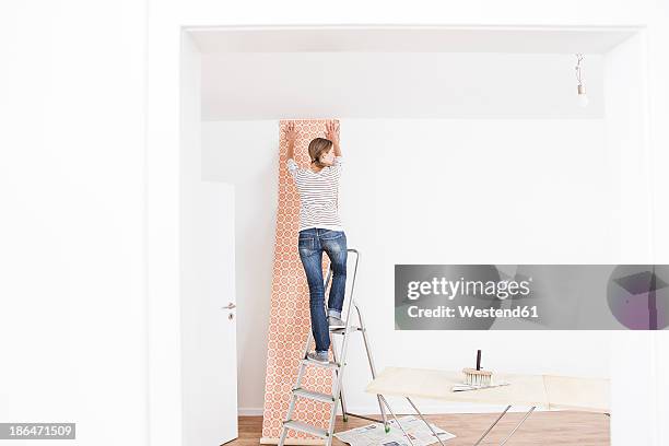 woman sticking wallpaper on wall - women for wallpaper stock pictures, royalty-free photos & images