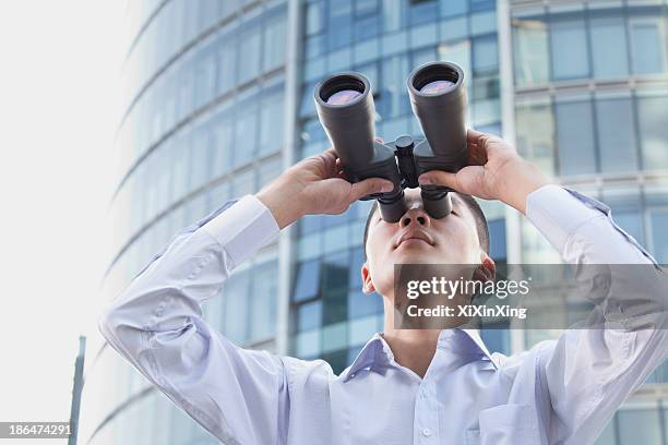 young businessman looking through binoculars - spy glass businessman stock pictures, royalty-free photos & images