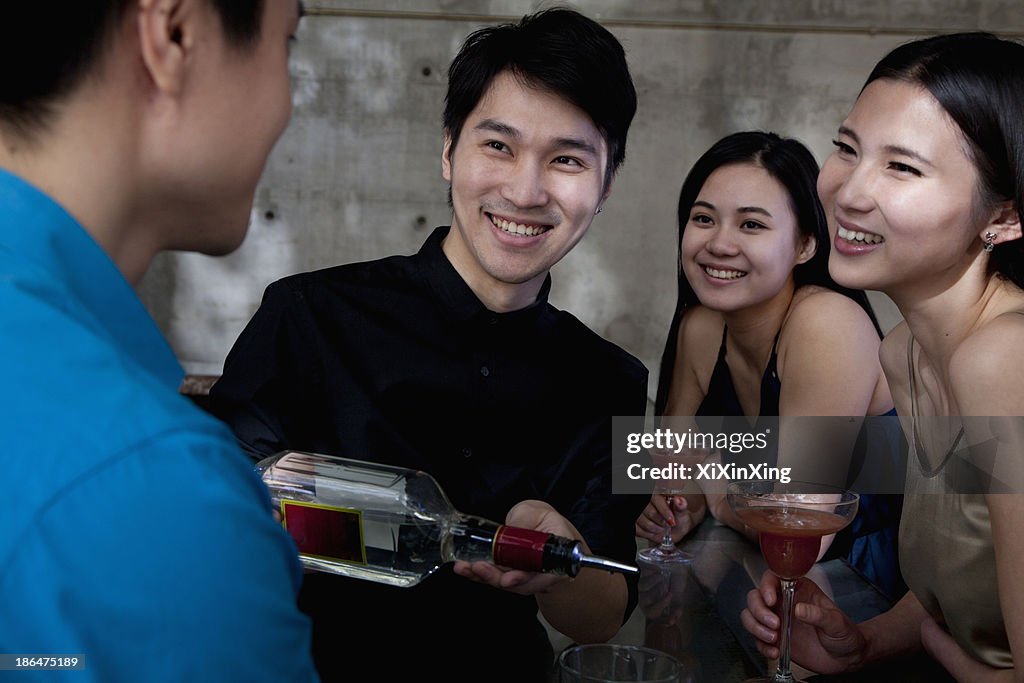 A young men bartender serving drinks to group of friends
