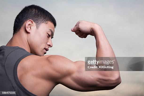 young man showing off his bicep muscles - flexing muscles ストックフォトと画像