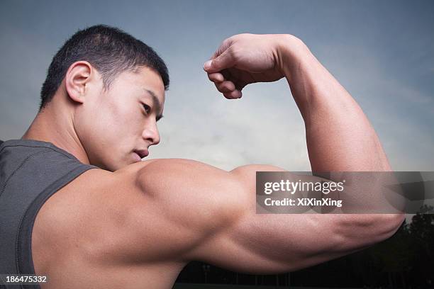 young man showing off his bicep muscles - flexing muscles foto e immagini stock