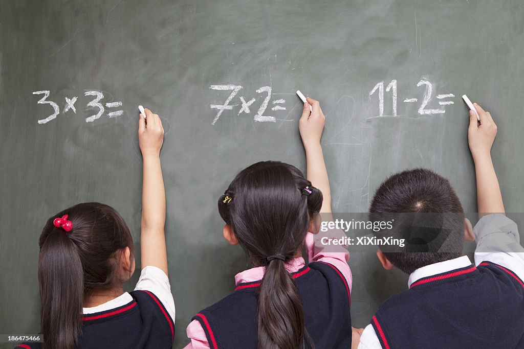 Three school children doing math equations on the blackboard