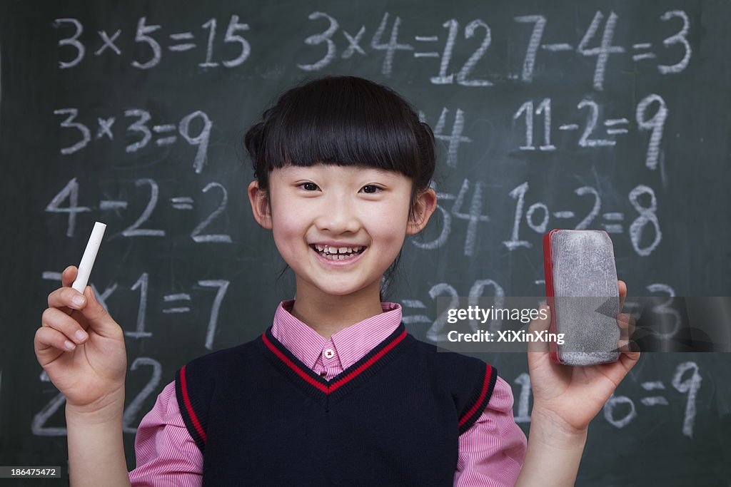 Portrait of schoolgirl in front of blackboard holding chalk and eraser