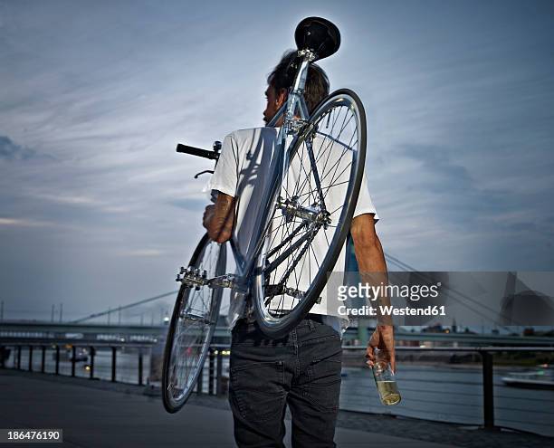 germany, cologne, young man carrying bicycle on shoulder with beer bottle - cologne bottle stock pictures, royalty-free photos & images