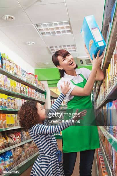 female sales clerk helping a little girl reach a cereal box - supermarket help stock-fotos und bilder