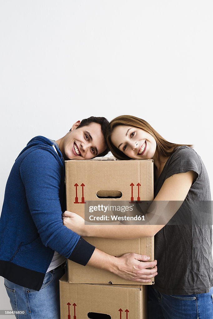 Germany, Munich, Portrait of young couple leaning on cardboard boxes, smiling