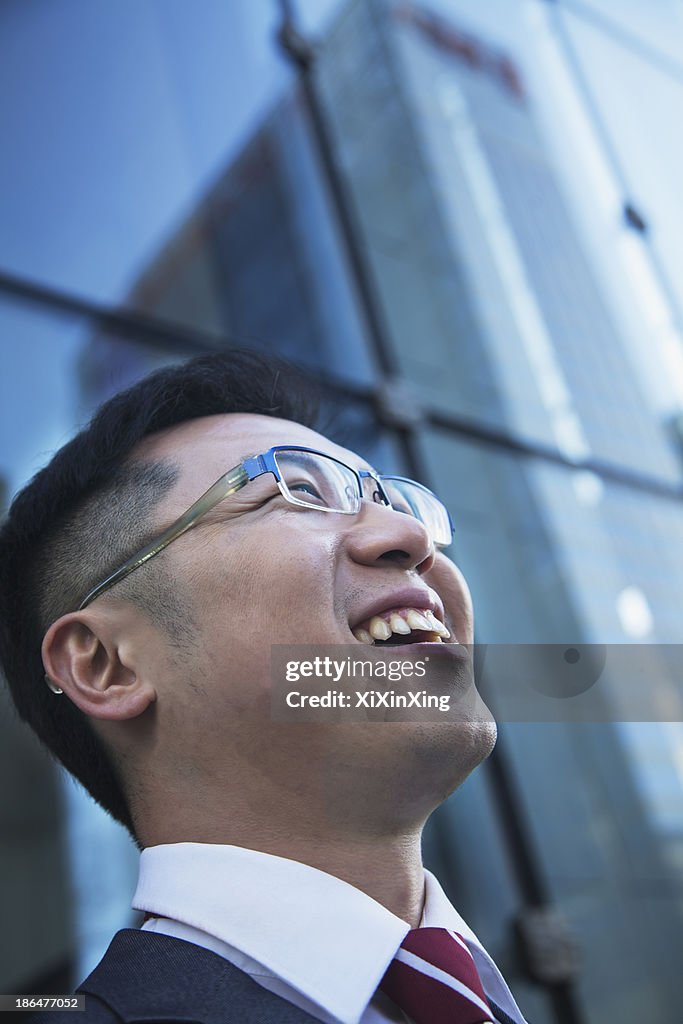 Close-up of smiling and laughing businessman looking up with glass reflection of skyscraper