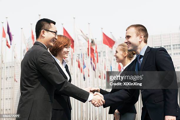 four smiling business people meeting and shaking hands outdoors, beijing - free trade agreement stockfoto's en -beelden