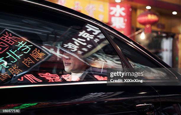 two business people sitting in the back of a car driving through the city at night, reflections of store signs on the car - china business stockfoto's en -beelden