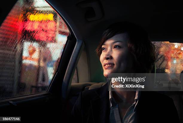 contemplative businesswoman looking out of car window through the rain at night in beijing - store sign stockfoto's en -beelden