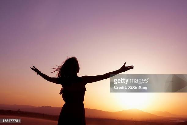serene young woman with arms outstretched doing yoga in the desert in china, silhouette - woman with arms outstretched stock pictures, royalty-free photos & images