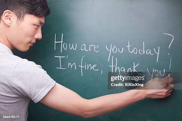 young man writing english sentences on the blackboard - lingua inglese foto e immagini stock