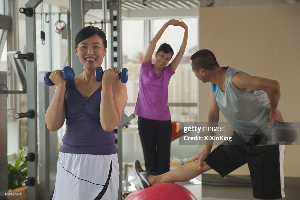 Mature woman lifting weights in the foreground, people exercising in the background