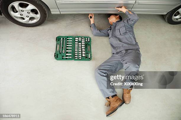 mechanic working on underside of car - car underside stock pictures, royalty-free photos & images