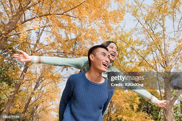 young couple piggyback in park - park couple piggyback stock pictures, royalty-free photos & images