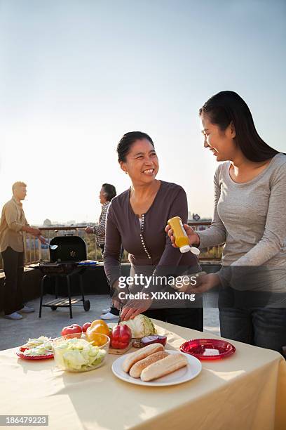 mother and daughter preparing hot dogs for barbeque, father and son preparing sausages on barbeque - barbeque party woman stock-fotos und bilder