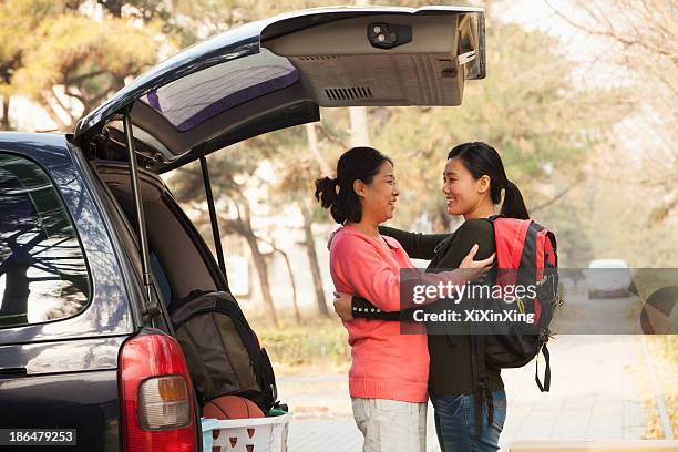 mother and daughter embracing behind car on college campus - basketball womens college foto e immagini stock