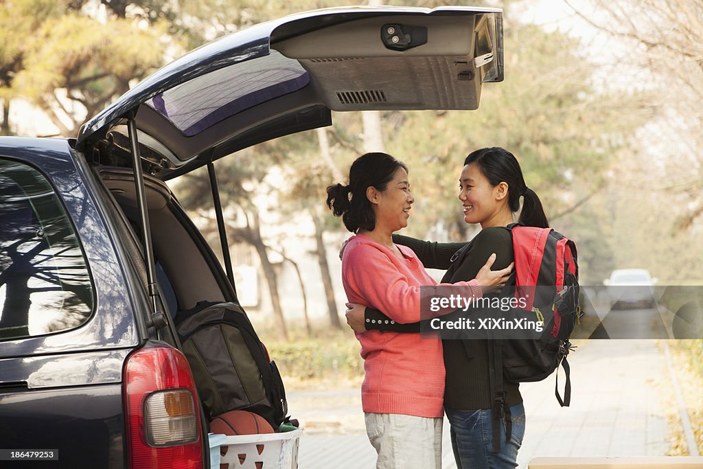 Mother and daughter embracing behind car on college campus