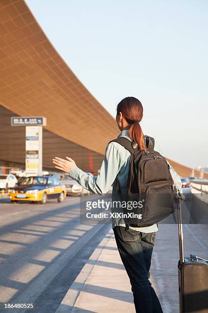 young traveler hailing a taxi at airport - hail foto e immagini stock
