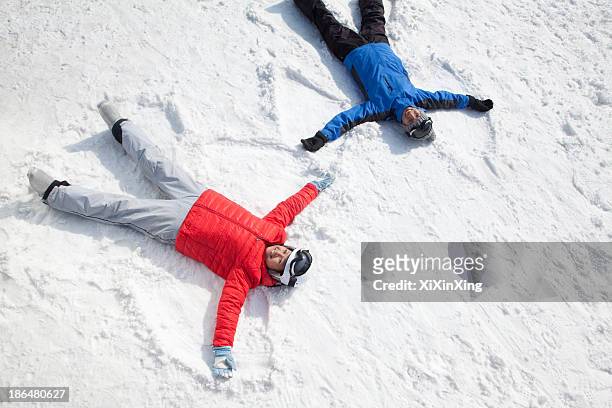 couple lying on snow making snow angel - sport d'hiver photos et images de collection