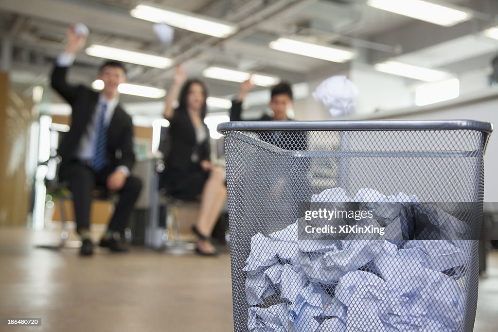 Three coworkers preparing to throw paper into waste basket