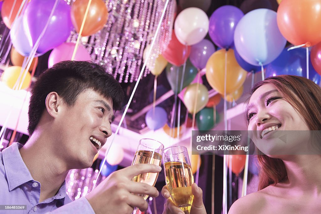 Two friends celebrating, toasting with champagne, nightclub in Beijing, balloons in the background