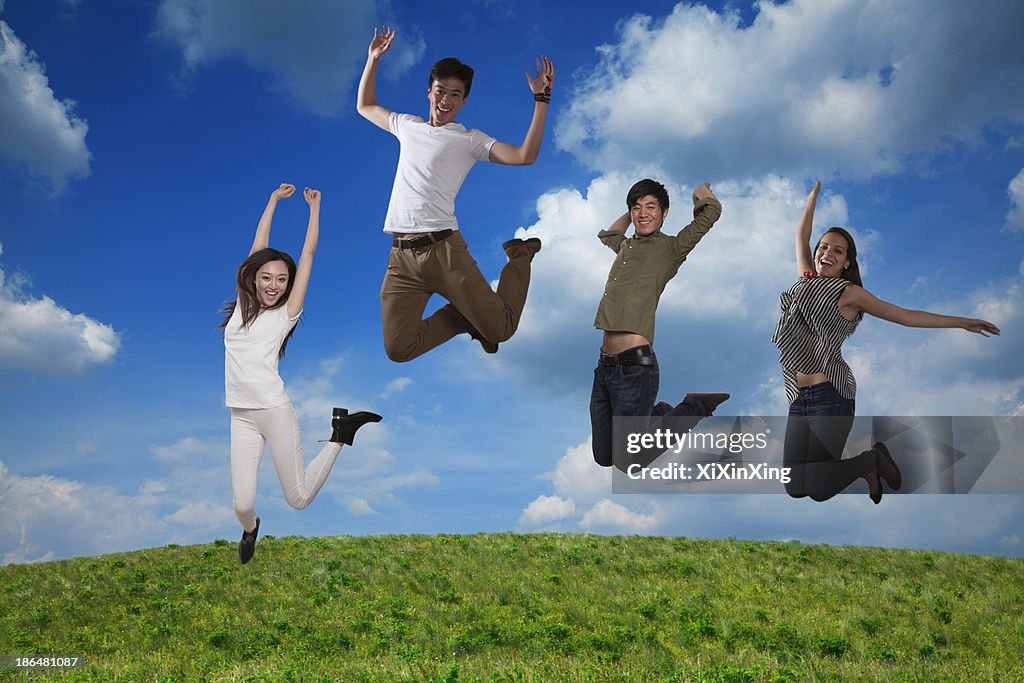 Four smiling friends jumping in mid-air, sky and cloud background