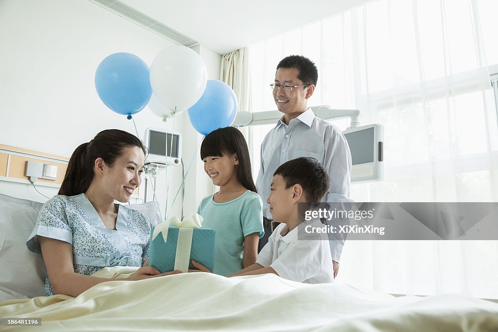 Father and children visiting their mother in the hospital, giving present and balloons