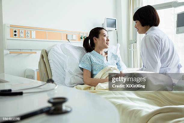 female doctor sitting on hospital bed and discussing with young female patient - chinese medicine stock-fotos und bilder