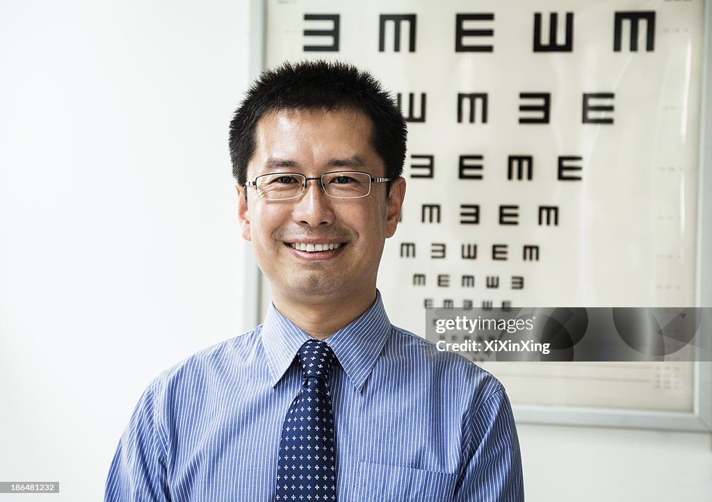 Portrait of smiling optometrist with an eye chart in the background