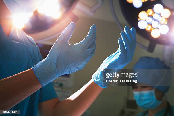 midsection view of hands in surgical gloves and surgical lights in the operating room - surgical glove stock pictures, royalty-free photos & images
