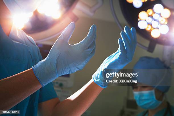 midsection view of hands in surgical gloves and surgical lights in the operating room - medical glove stock pictures, royalty-free photos & images