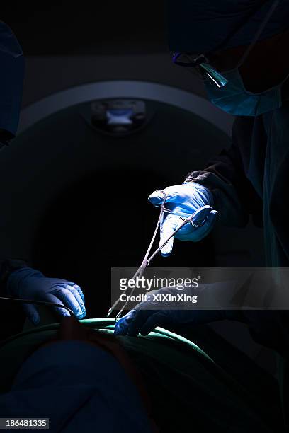 surgeon looking down, working, and holding surgical equipment with patient lying on the operating table, dark - operating table stock pictures, royalty-free photos & images
