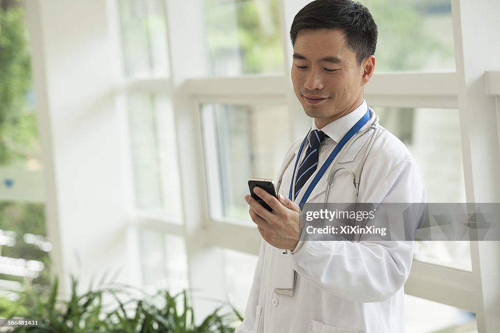 Smiling doctor looking down at his phone in the hospital lobby