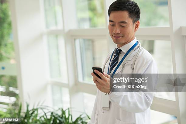 smiling doctor looking down at his phone in the hospital lobby - doctor looking down stock pictures, royalty-free photos & images