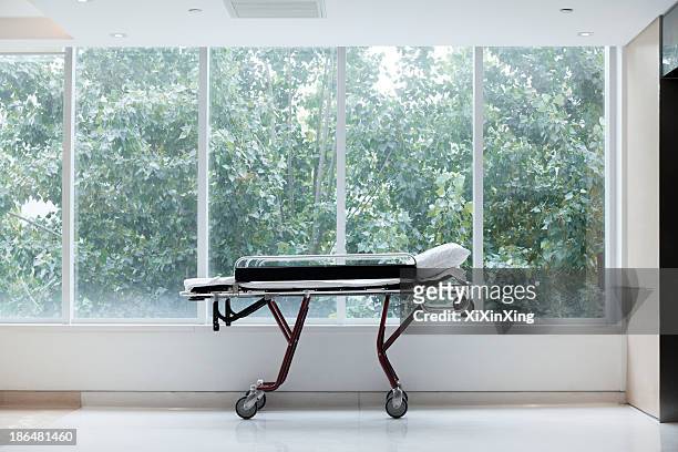 empty stretcher in a hospital by glass windows, no people - hospital gurney stock pictures, royalty-free photos & images