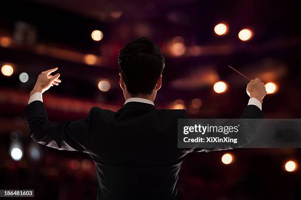 young conductor with baton raised at a performance, rear view - dirigent stock-fotos und bilder