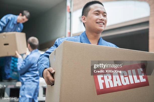 movers unloading a moving van and carrying a fragile box - moving service imagens e fotografias de stock