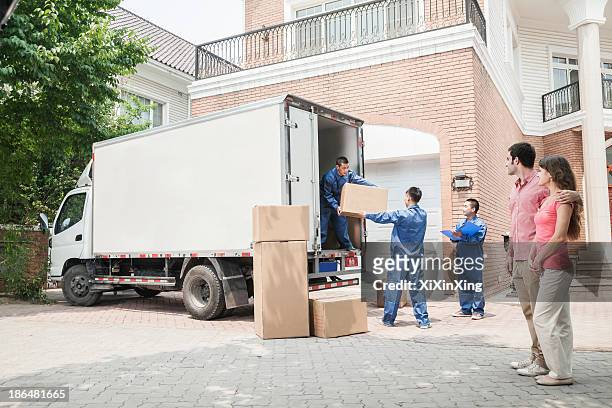 young couple watching movers move boxes from the moving van - removal men imagens e fotografias de stock