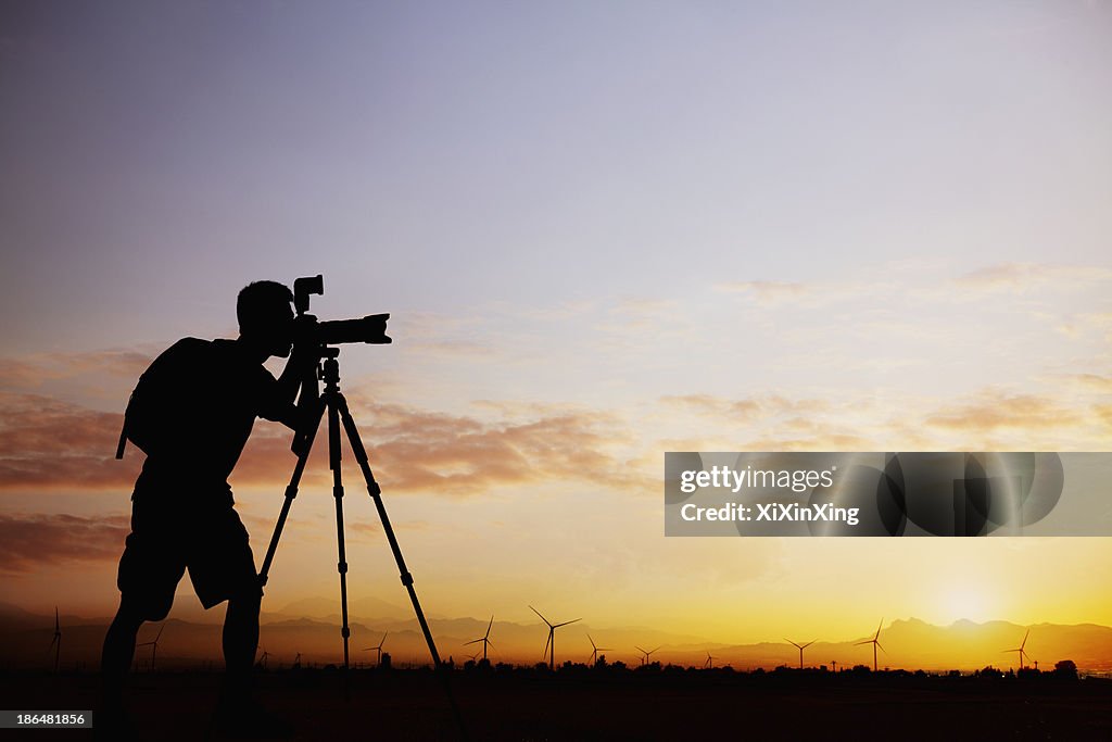 Silhouette of man taking photos with his camera at sunset with a dramatic sky