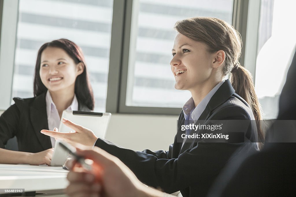 Two businesswomen smiling, discussing, and gesturing during a business meeting