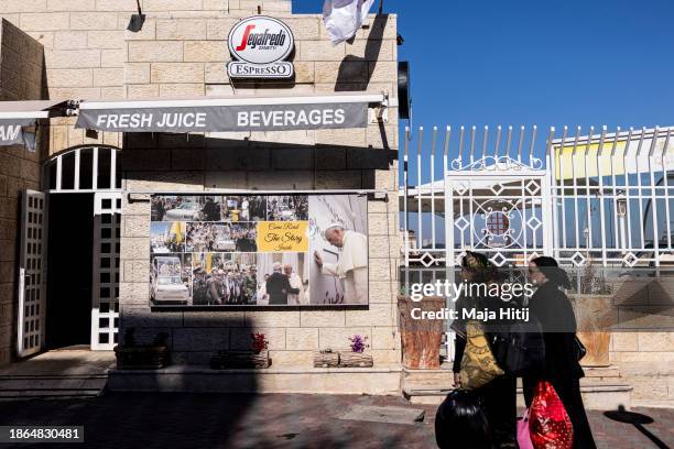 Palestinian women walk past a coffee shop with a pictures of Pope Francis on December 18, 2023 in Bethlehem, West Bank. Last month, Christian...