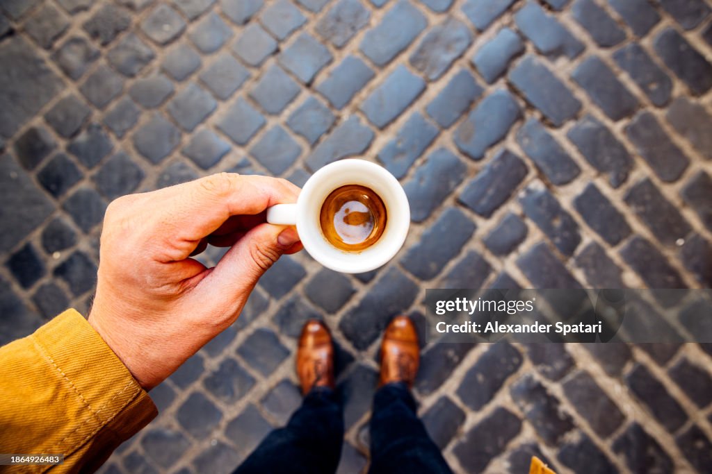 Man drinking espresso on the cobblestone street in Rome, personal perspective view, Italy